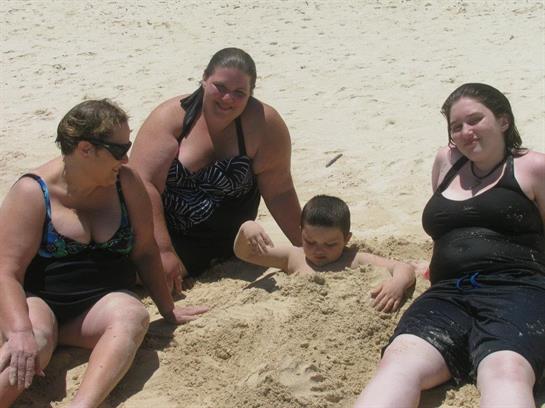 Four family members relax on a sandy beach, playfully burying one another in the sun during summer.