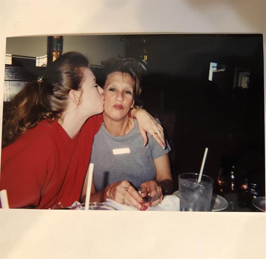 A daughter affectionately kisses her mother at a cozy restaurant while they share a meal.