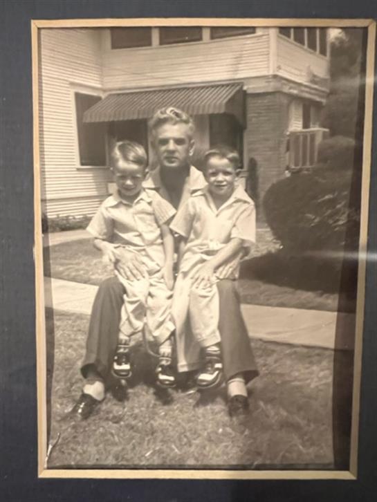 Two young boys happily sit on a woman's lap in the front yard, enjoying family time.
