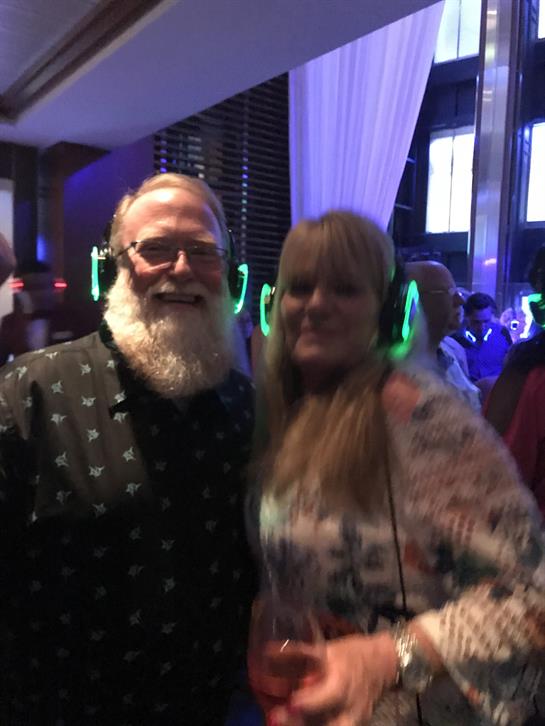 Friends dance and socialize at a silent disco, wearing glowing headsets in a lively setting.