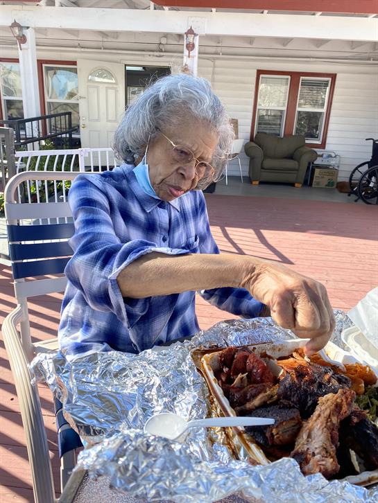 An elderly woman enjoys the pleasant weather while serving herself a meal outside.
