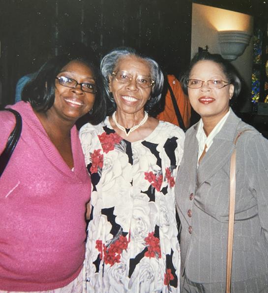 Three women share joyful smiles at a family gathering, enjoying each other's company and warmth.