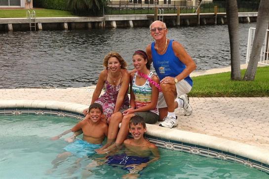 A family enjoys quality time together by their backyard pool under a clear sky.