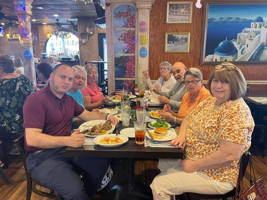 A lively group is gathered at a restaurant table enjoying their meal and sharing smiles.