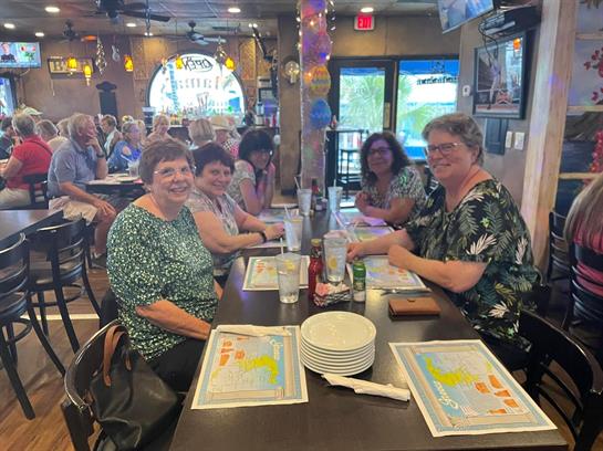 A group of friends gathers at a restaurant with plates and drinks, enjoying each other's company.