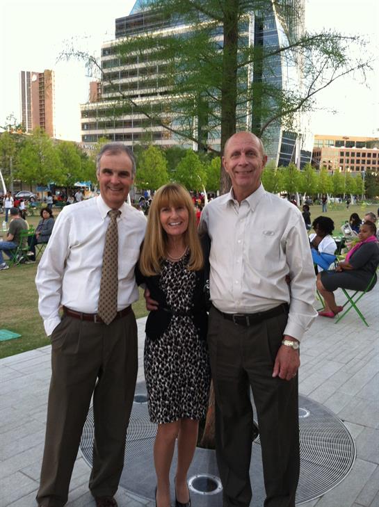 Three friends smile together in a sunny park, enjoying each other's company.