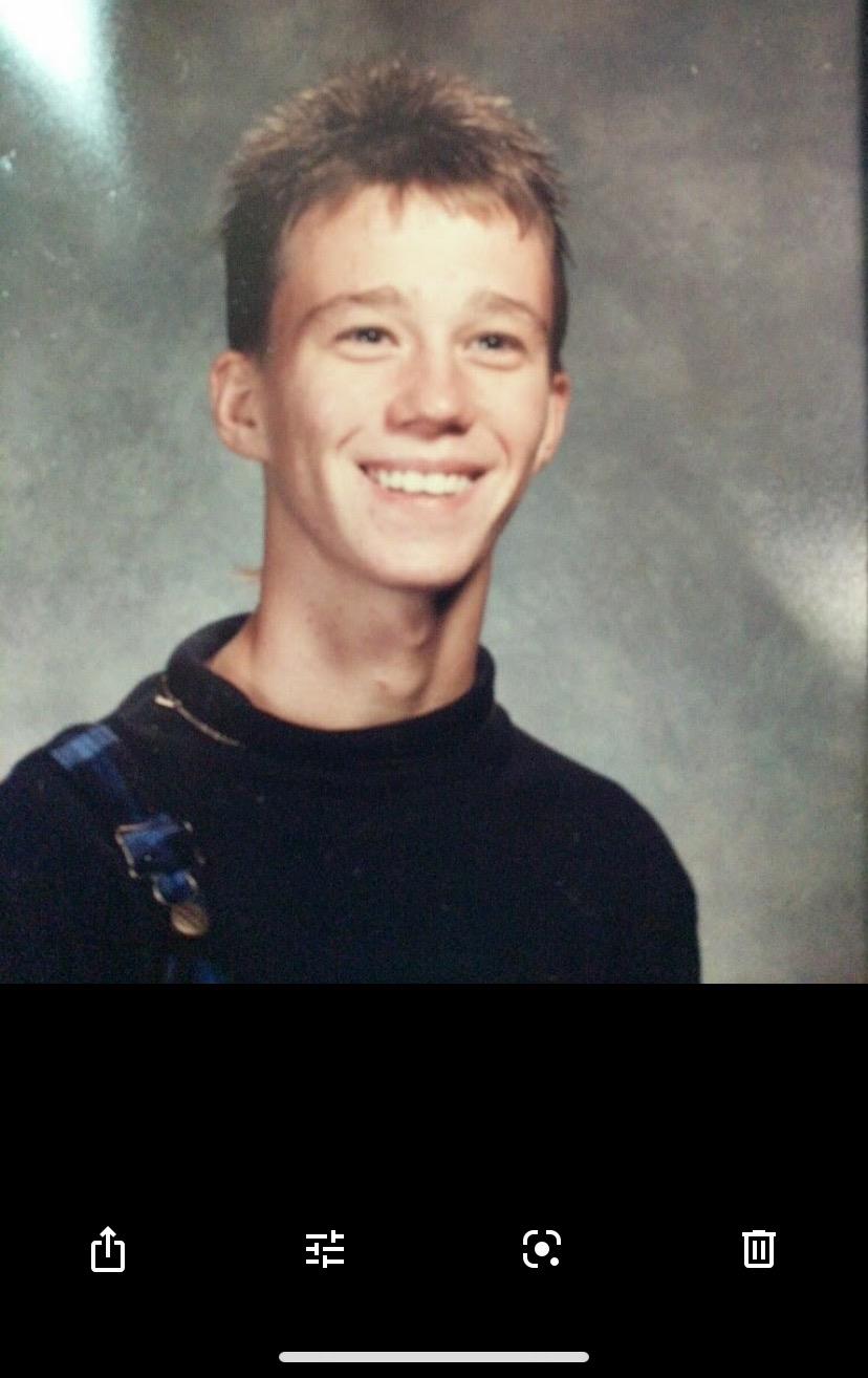 A cheerful young man wearing a black sweater smiles brightly for his school portrait.