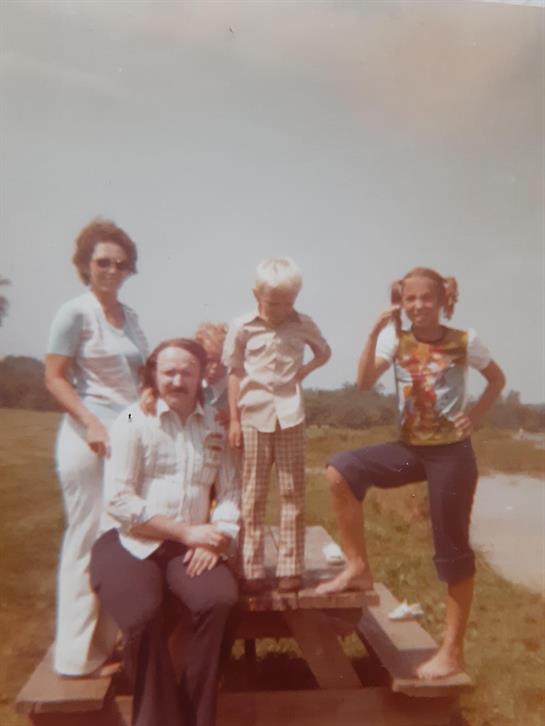 A cheerful family enjoys a sunny day outdoors, surrounded by greenery, with children playing nearby.
