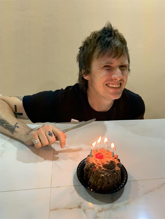 A young man joyfully cuts a cake adorned with lit candles, celebrating a special occasion.