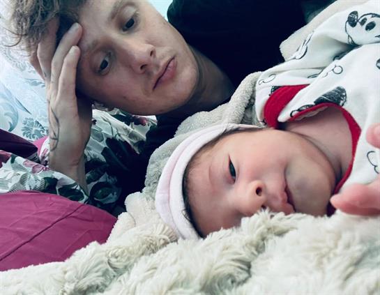 A father lies next to his newborn, both calmly relaxing on a soft surface, enjoying togetherness.