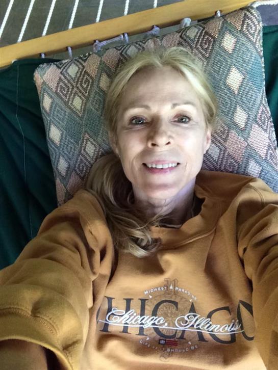 A woman smiles on the couch, clad in a comfy sweatshirt, enjoying her surroundings.