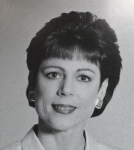 A confident woman poses in a professional setting, showcasing a polished look and a warm smile.