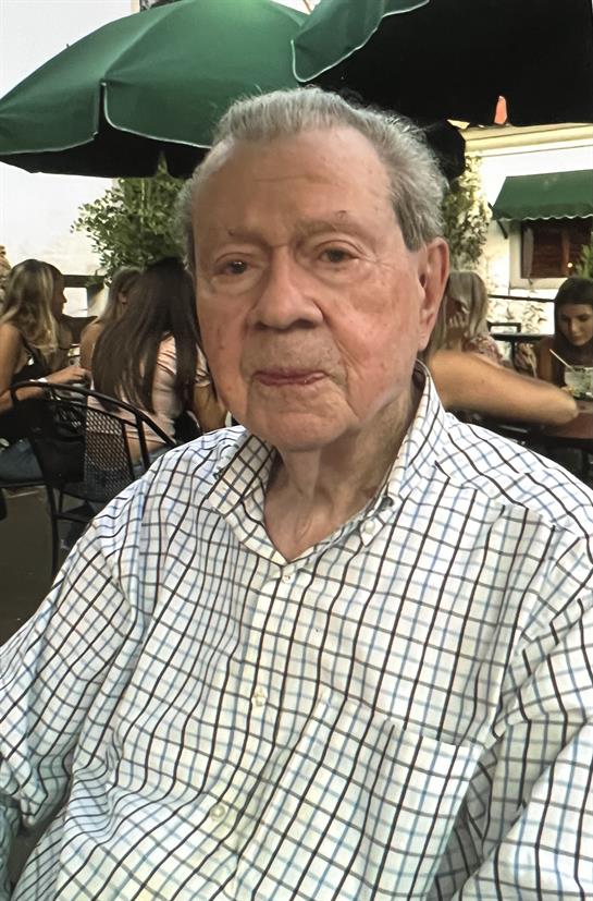 An elderly man relaxes at an outdoor café, surrounded by friends on a pleasant evening outing.