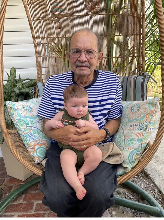 Elderly man cherishes quiet time holding a baby in a swing, surrounded by greenery.