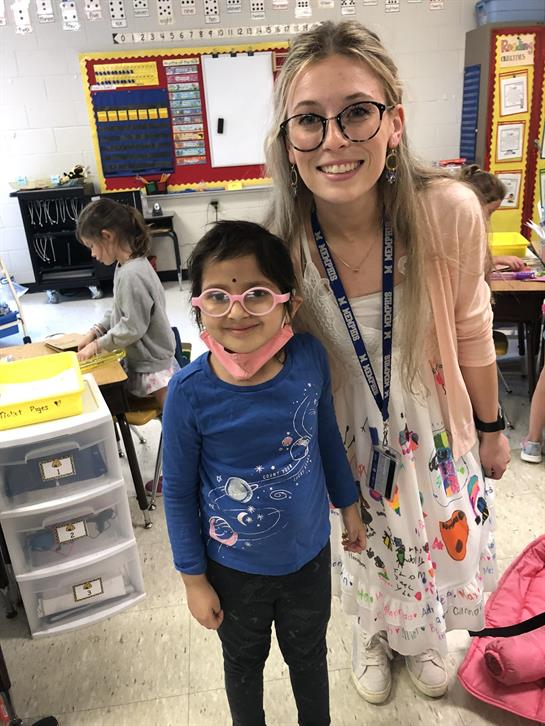 A happy student and teacher engage in fun activities in a colorful classroom.