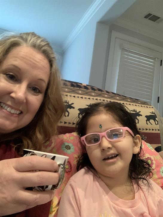 Woman and girl smile joyfully while sharing a cup in a cozy living room setting.