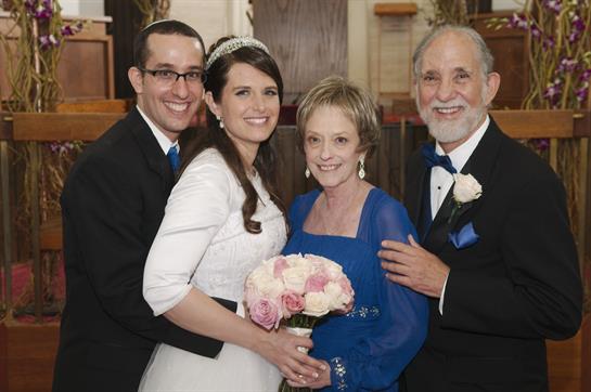 A joyful couple poses with their parents, all smiling and sharing a special moment together.