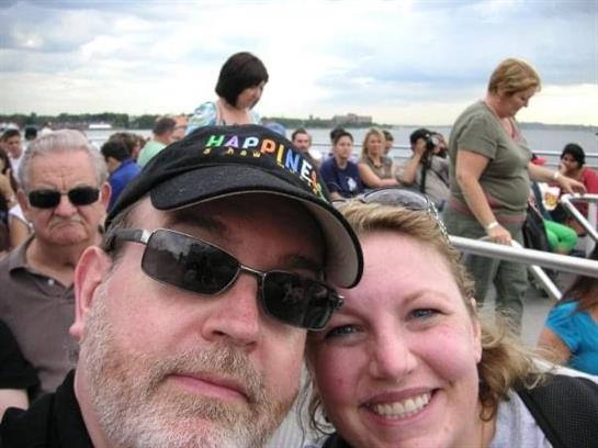 A couple smiles for a selfie while embarking on a boat trip with friends around them.