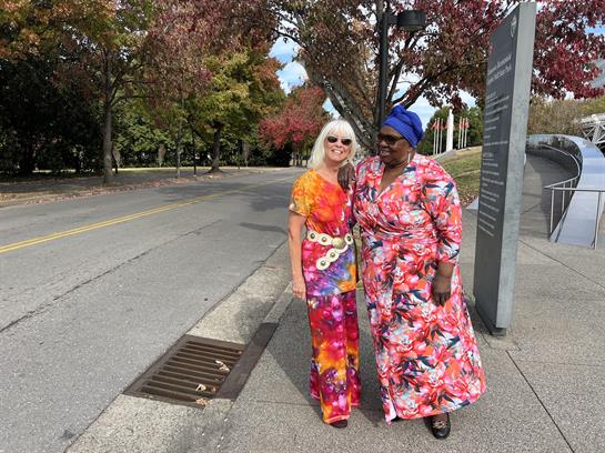 Two women dressed in vibrant attire enjoy a stroll in a scenic park filled with colorful trees.