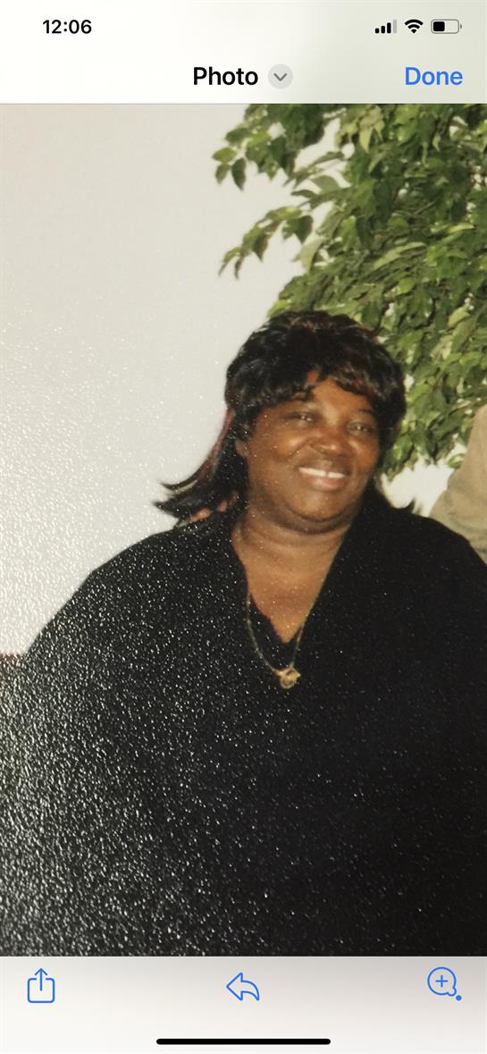 Woman with long hair smiles brightly while seated in a relaxed indoor setting adorned with plants.