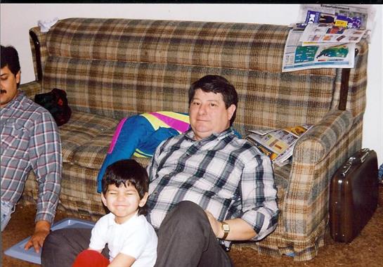 A young boy smiles while sitting on the floor next to an older man in a living room.