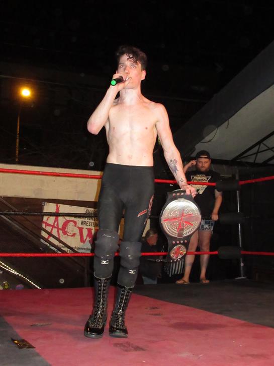 Competitor holds a championship belt and gives a speech proudly in the ring.