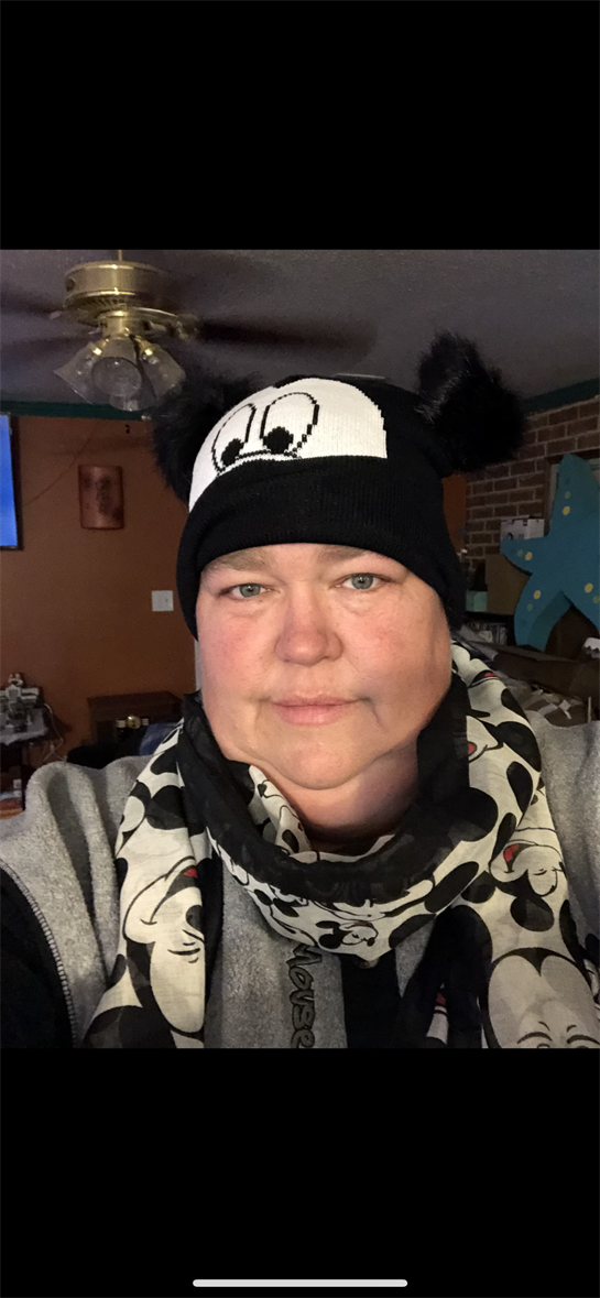 A woman is dressed in a black hat with ears and a matching scarf in a homey atmosphere.