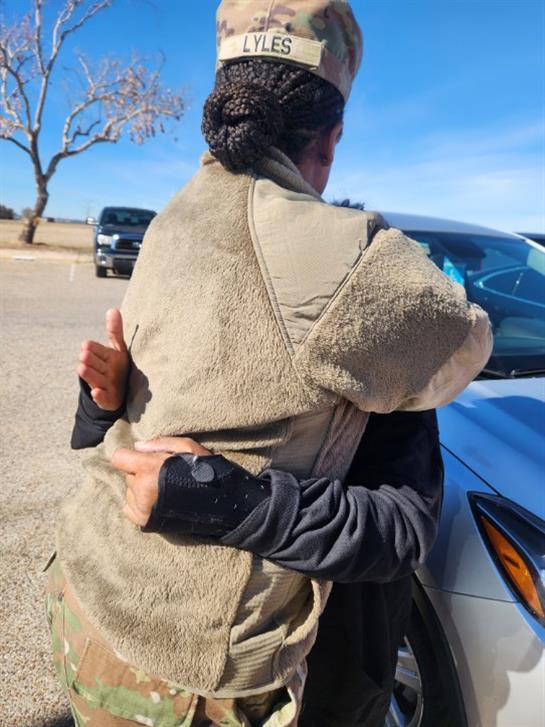 Two friends share a heartfelt hug outside during a warm, sunny day in a rural landscape.