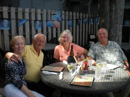 Four friends gather around a table sharing food and laughter in a vibrant outdoor space.