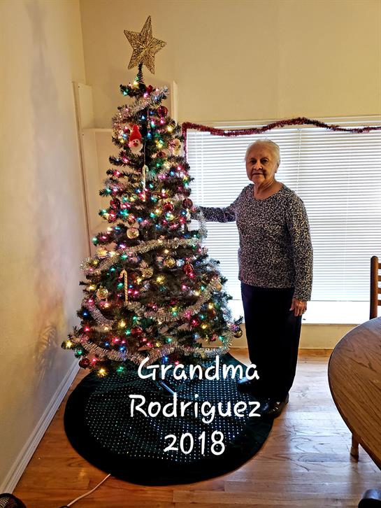 Grandma stands proudly by the decorated Christmas tree in the cozy living room.