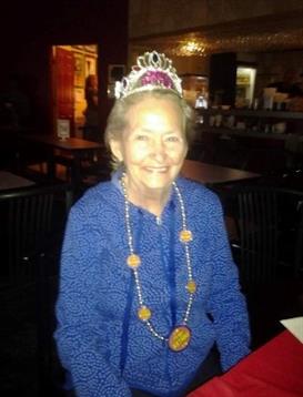 Cheerful elderly woman smiles while celebrating her birthday with festive attire in a dining venue.