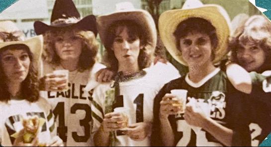 Three women in casual wear and cowboy hats enjoy a festive outdoor event with cups.