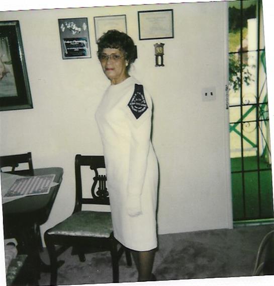 A woman poses elegantly in a white dress, showcasing a stylish aesthetic in a cozy indoor space.