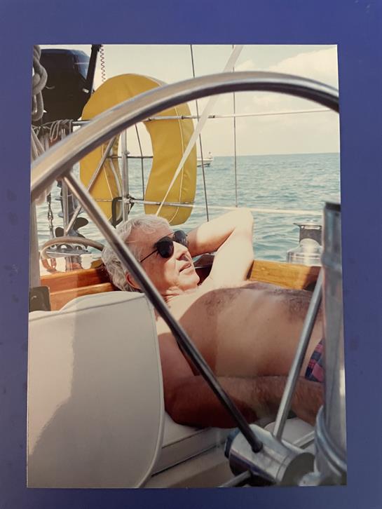 A sailor lounges on a sailboat, soaking up the sun while surrounded by serene waters.