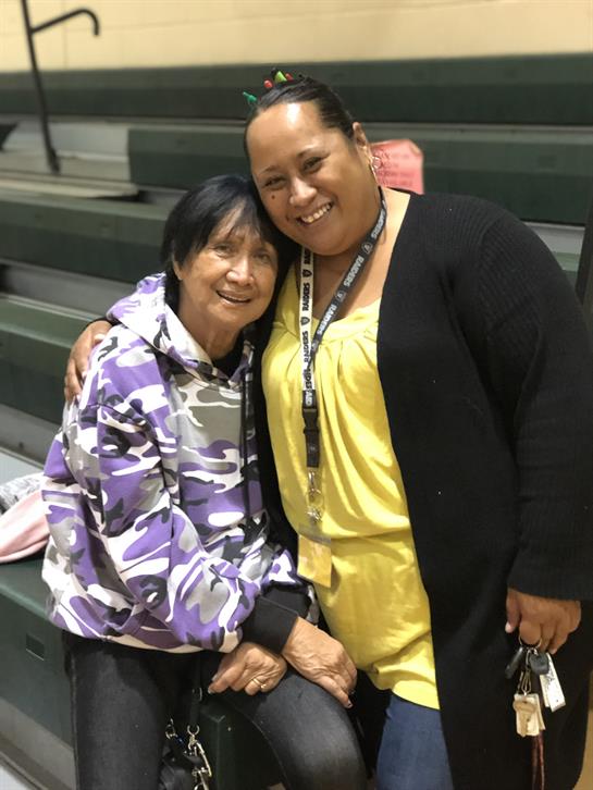 Two family members share a warm embrace, smiling happily in a gymnasium setting.