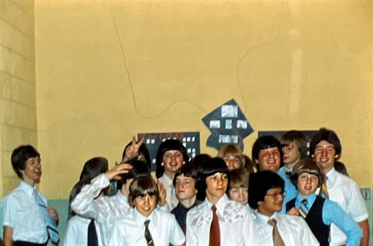 Students dressed in formal shirts and ties celebrate together in a lively school atmosphere.