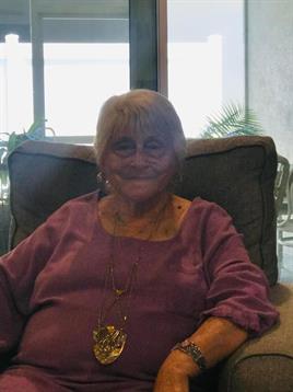 An elderly woman enjoys her time sitting comfortably in a chair, surrounded by natural light.