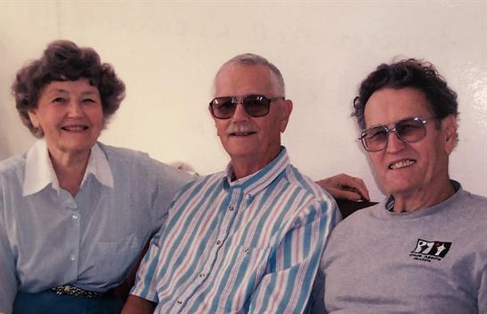 Three senior friends sit close together, smiling warmly while enjoying a relaxed moment indoors.