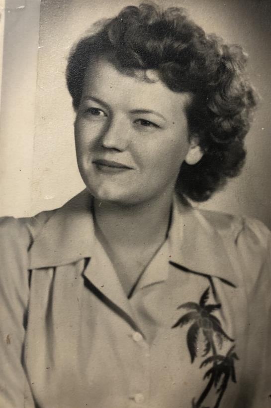 Young woman with curly hair smiles gently, wearing a floral blouse in a vintage setting.