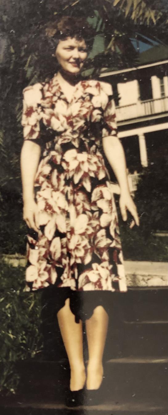 A woman poses in a floral dress, showcasing classic fashion outdoors in a vintage environment.