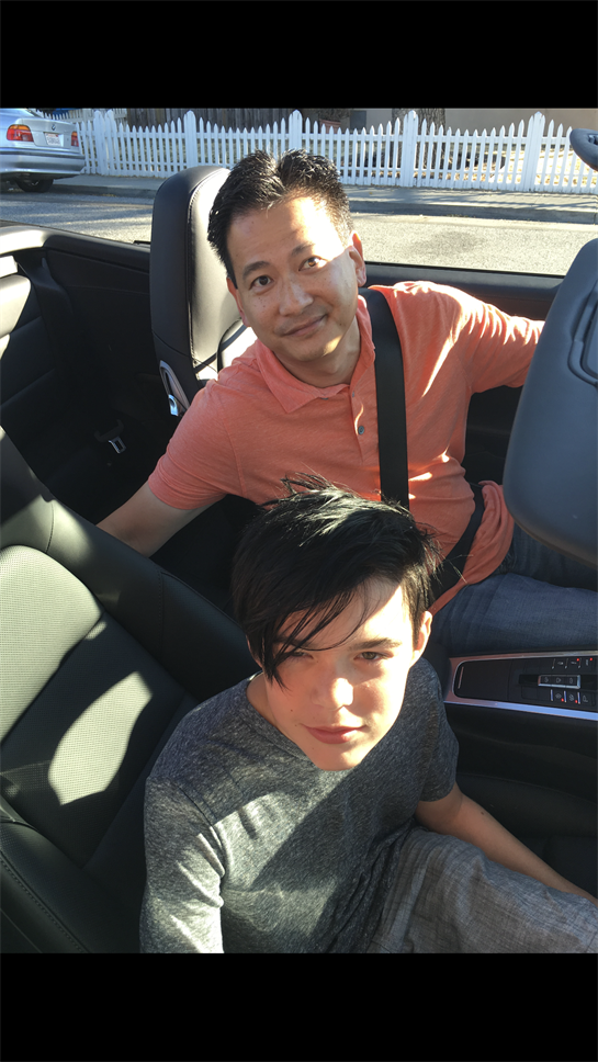 A father sits in the front seat while his son looks confidently from the backseat, both relaxed.