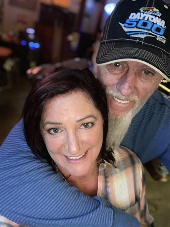 A happy couple shares a warm embrace while smiling at each other in a vibrant atmosphere.