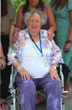 Elderly woman in wheelchair surrounded by family members in a sunny garden.