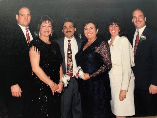 Six friends smile in elegant outfits, celebrating a special event together.