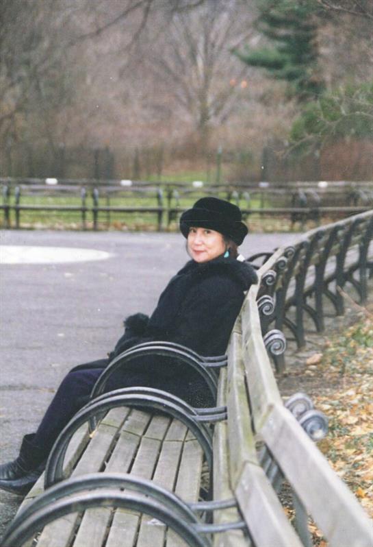 A woman dressed in black relaxes on a bench in a quiet park surrounded by autumn colors.