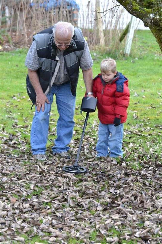 An adult teaches a child how to use a metal detector among fallen leaves in a forest.