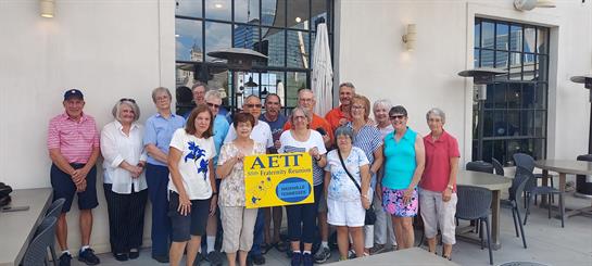 Friends celebrate together outside a cafe under a clear sky on a warm summer day.