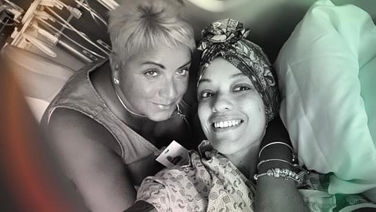 Two women share a cheerful expression while taking a close-up selfie in a cozy indoor setting.