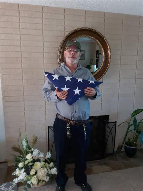 A man displays a folded flag while standing in his living room near a fireplace.