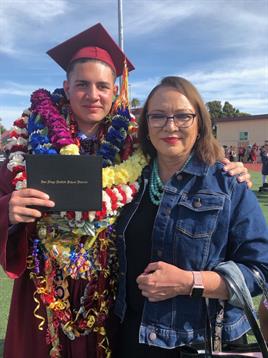 Young graduate proudly shows diploma with a supportive family member at graduation.